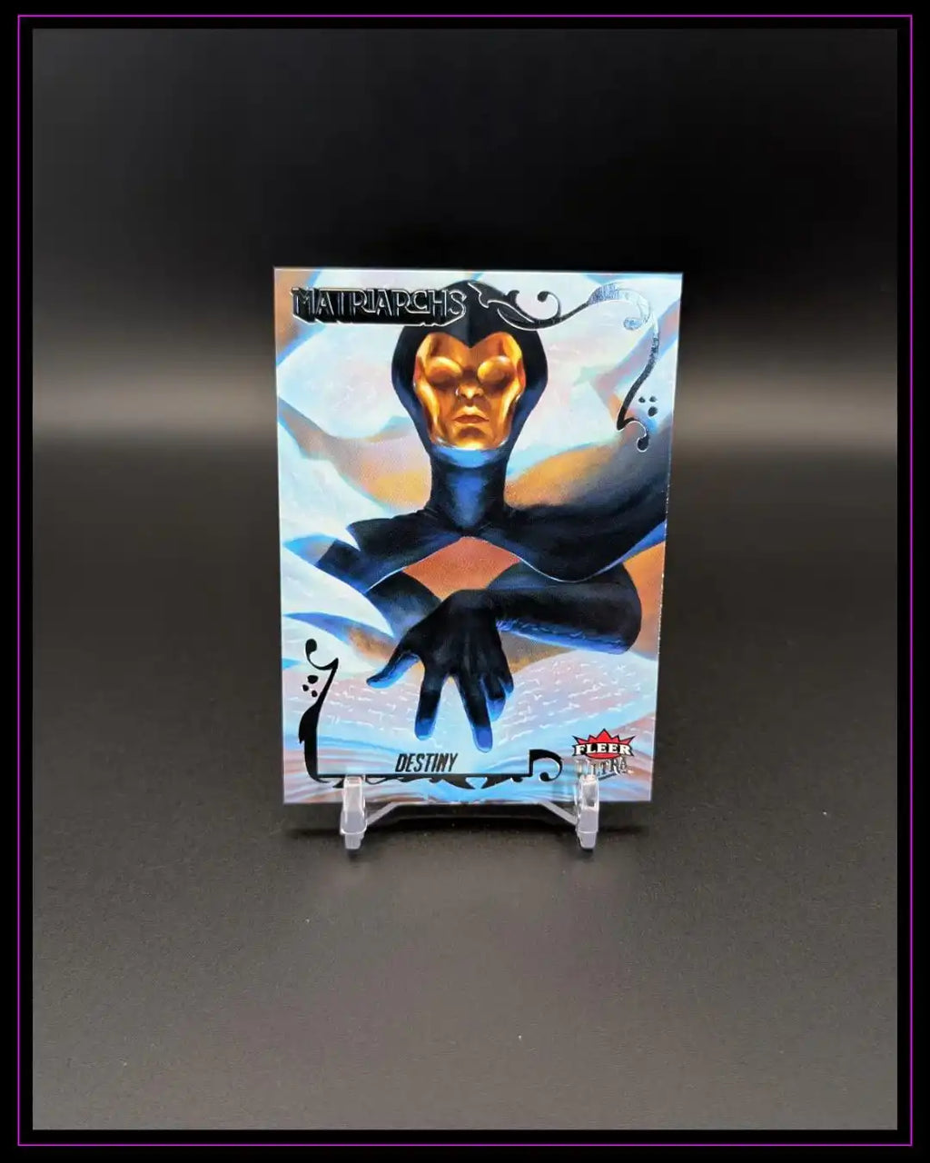 Trading Card mit Illustration der Figur Destiny, goldene Maske, schwarzes Kostüm, Aufschrift Matriarchs